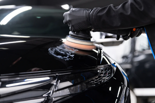 Detailer polishing a black car hood with a machine polisher before applying ceramic protection.