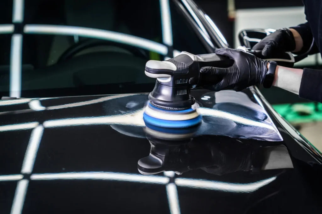 Detailer polishing a black car hood with a machine polisher before applying ceramic protection.